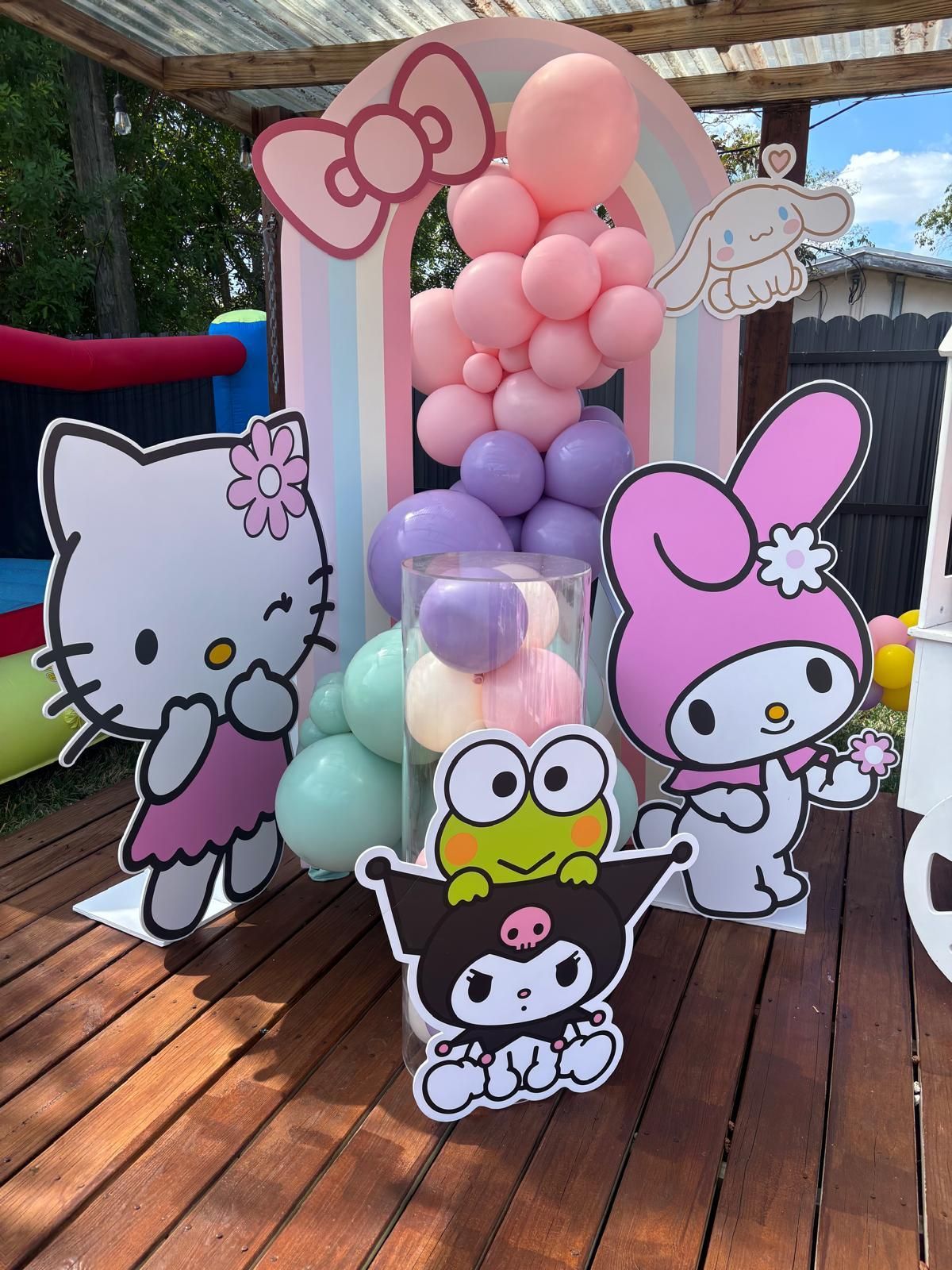 Sanrio-themed party decor with a rainbow arch, balloon clusters, and character cutouts including Hello Kitty and Kuromi.