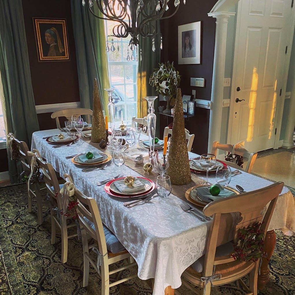 Formal dining room with a long table set for a meal. Sunlight streams through a window, illuminating decorations.