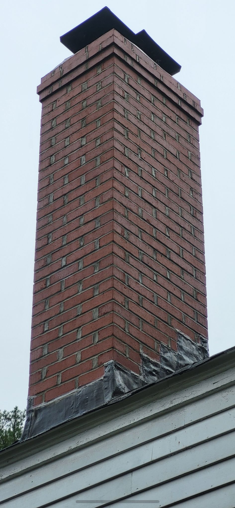 A tall brick chimney is sitting on top of a white house.