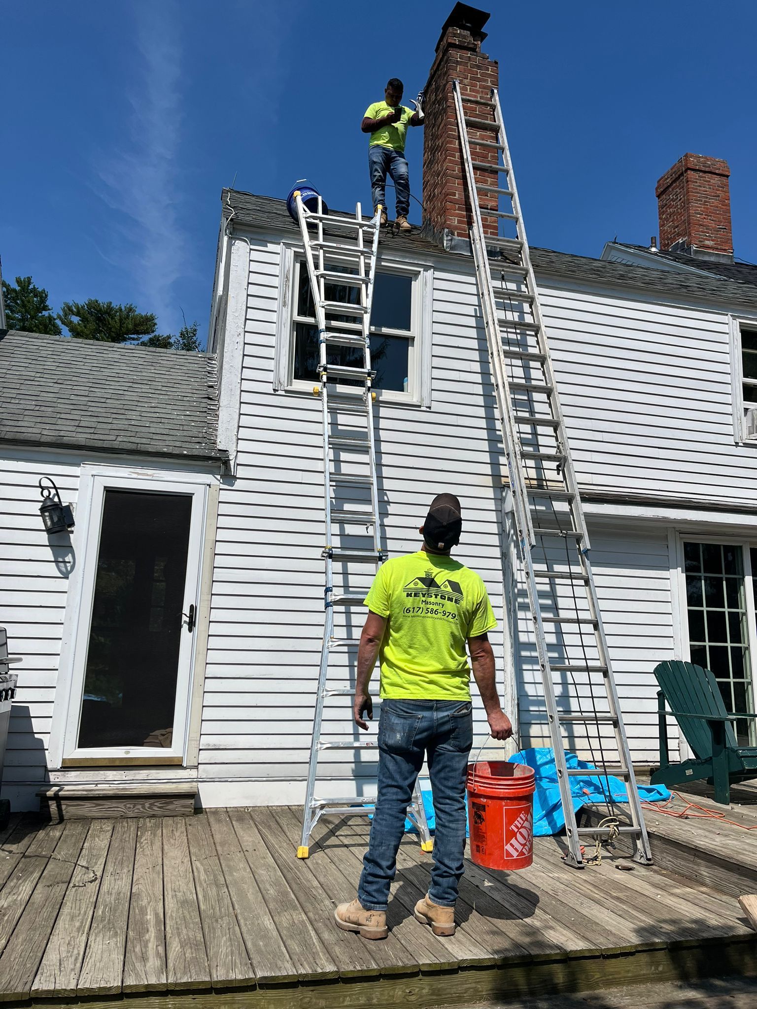 A man is standing on a ladder on the roof of a house.