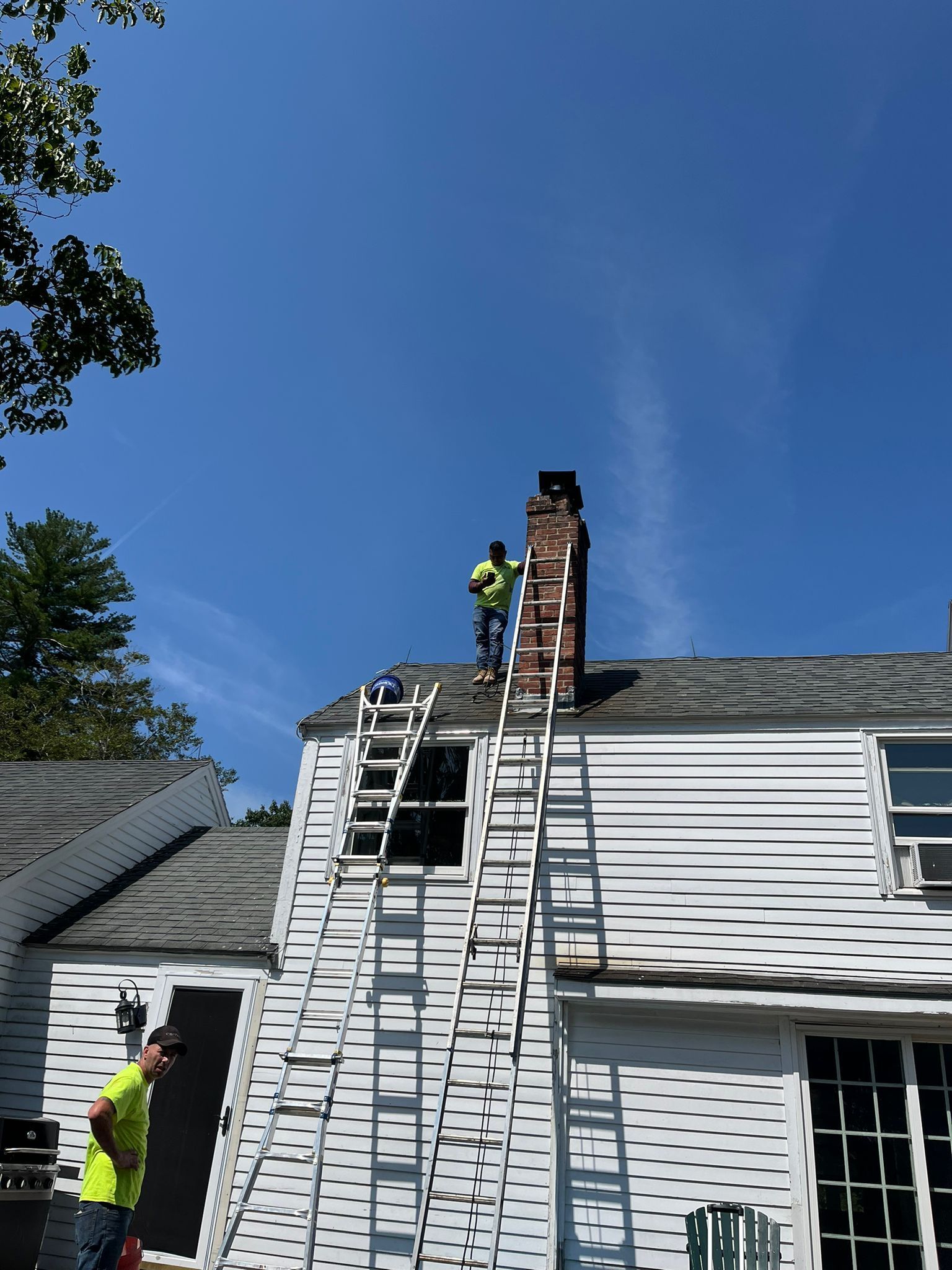 Two men are working on the roof of a white house.