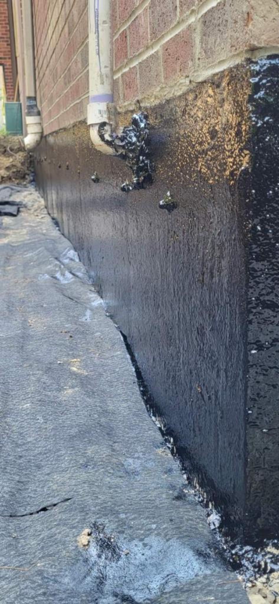 A drainage system is being installed on the side of a brick building.