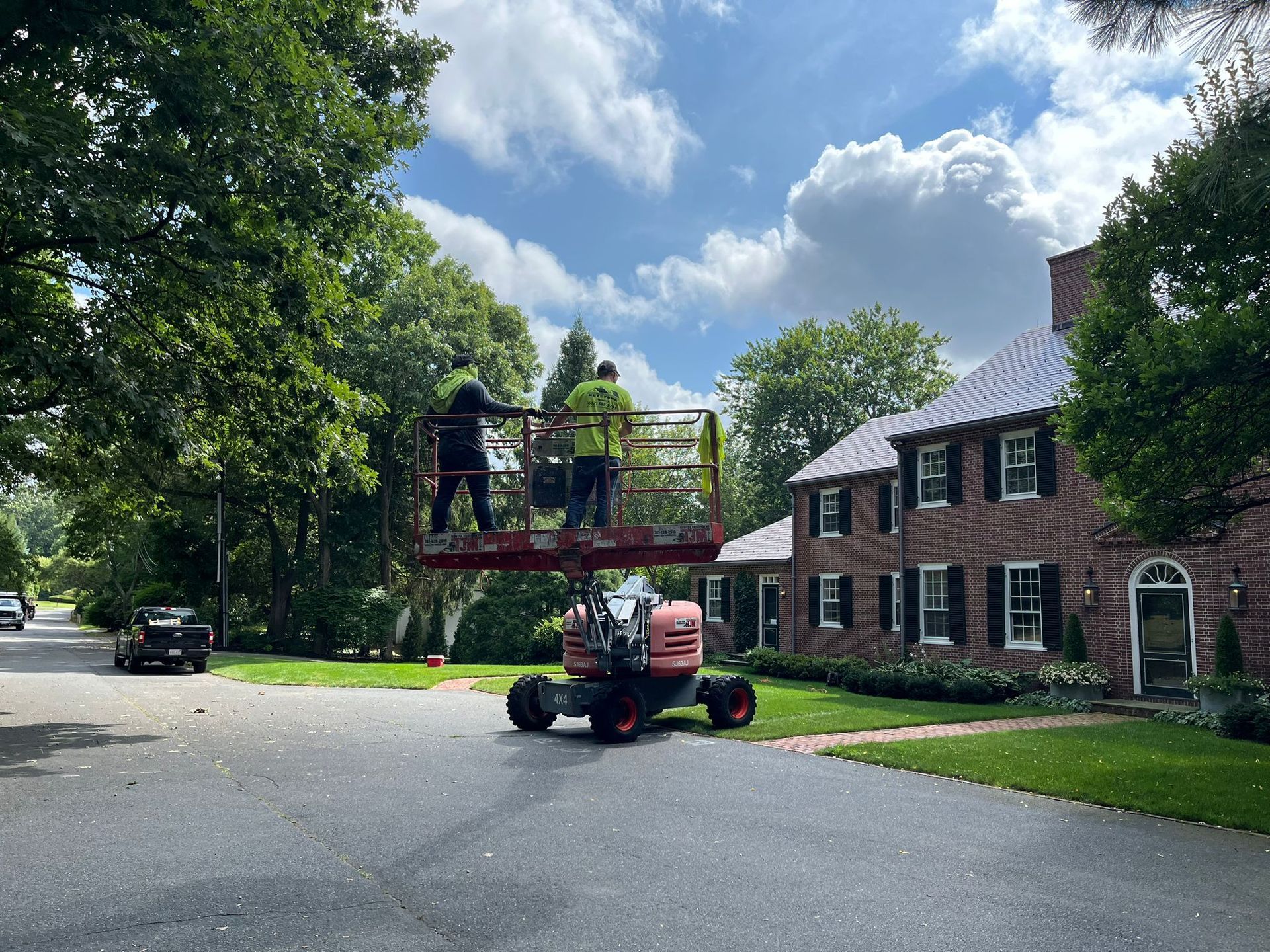 A man is standing on a lift in front of a brick house.