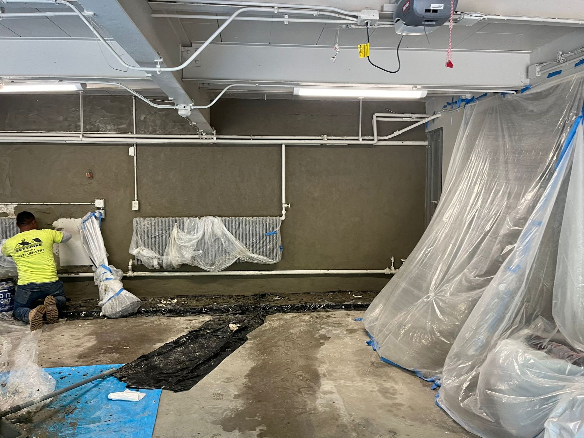 A man is working on a wall in a building covered in plastic.