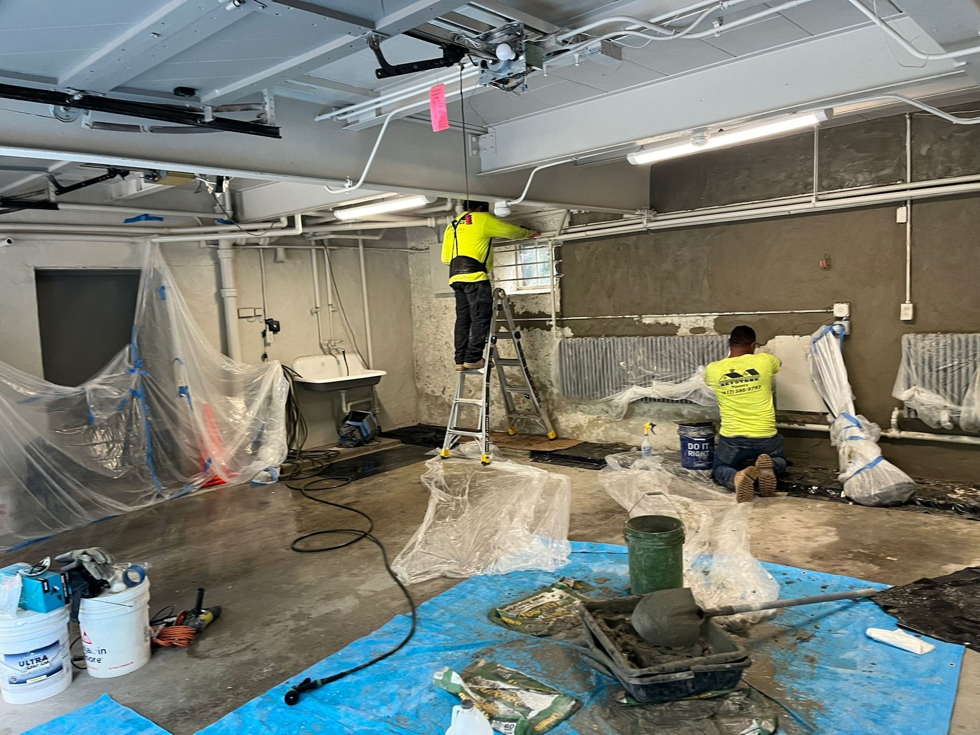 Two men are working on a wall in a room.