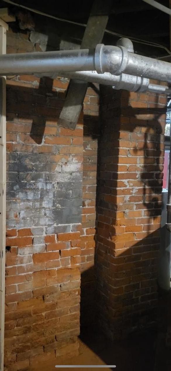 A brick wall with pipes coming out of it in a basement.