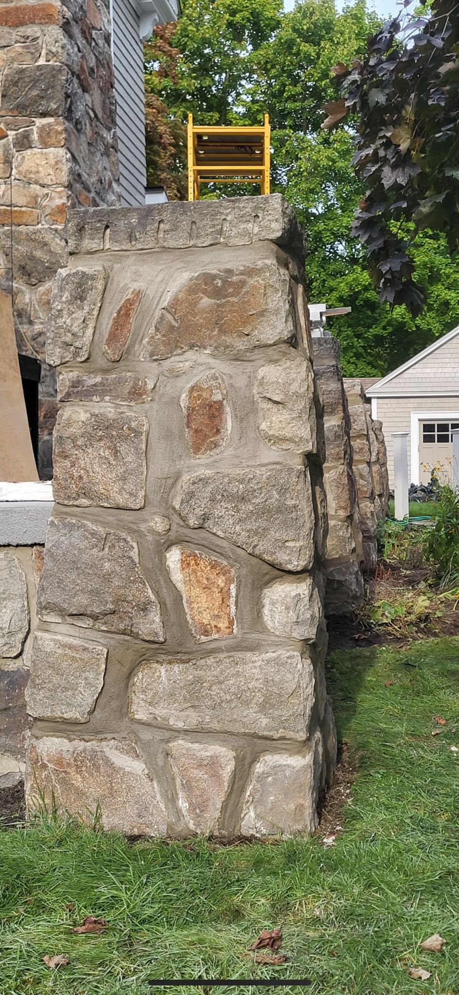 A yellow ladder is sitting on top of a stone wall