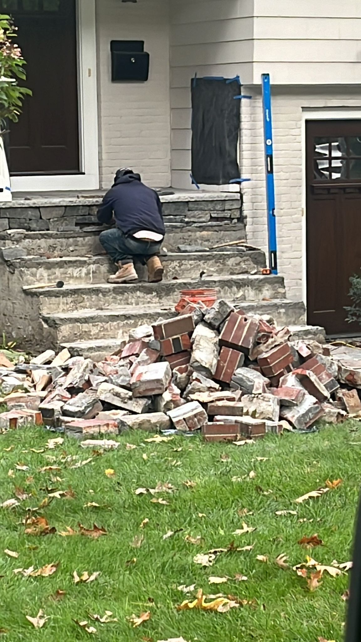 A man is kneeling on a pile of bricks in front of a house
