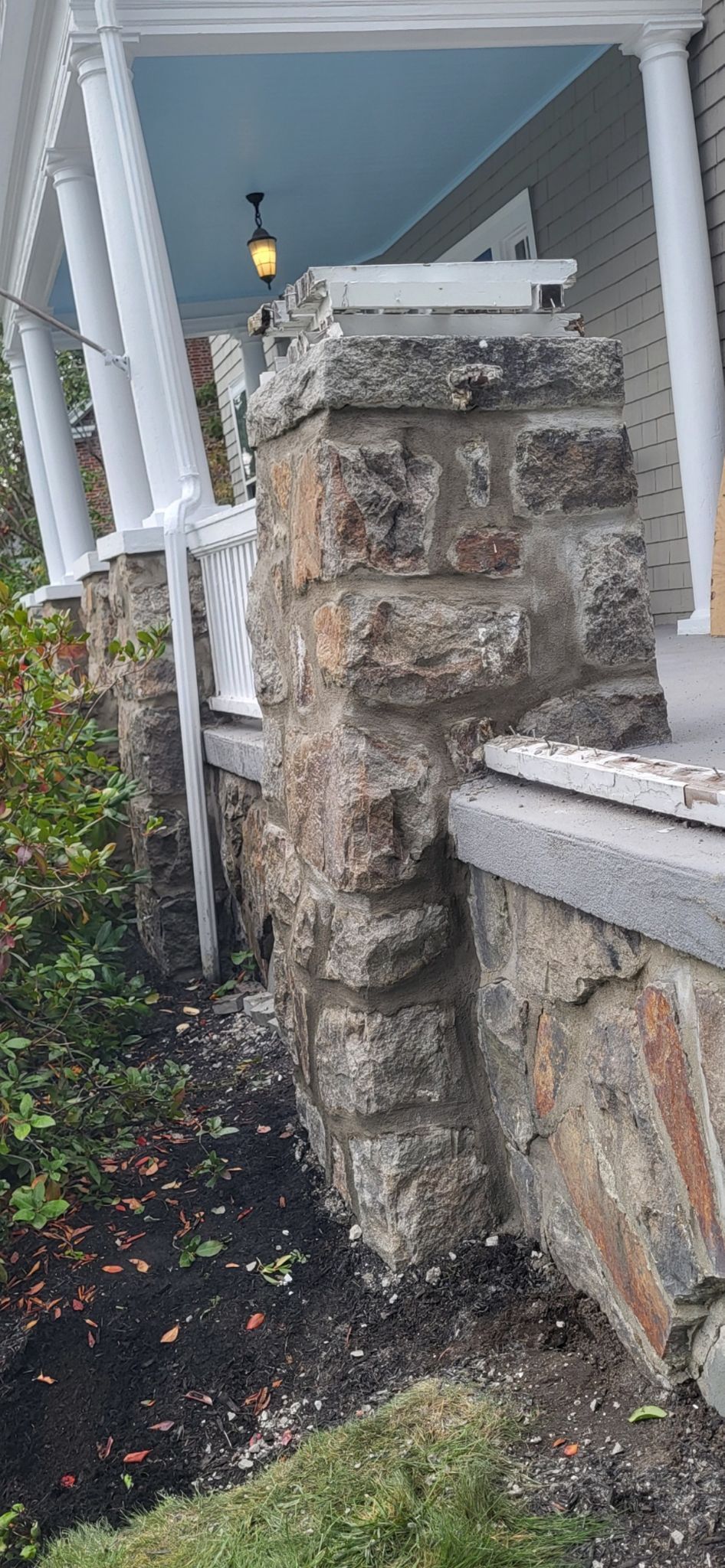 A stone wall next to a porch of a house
