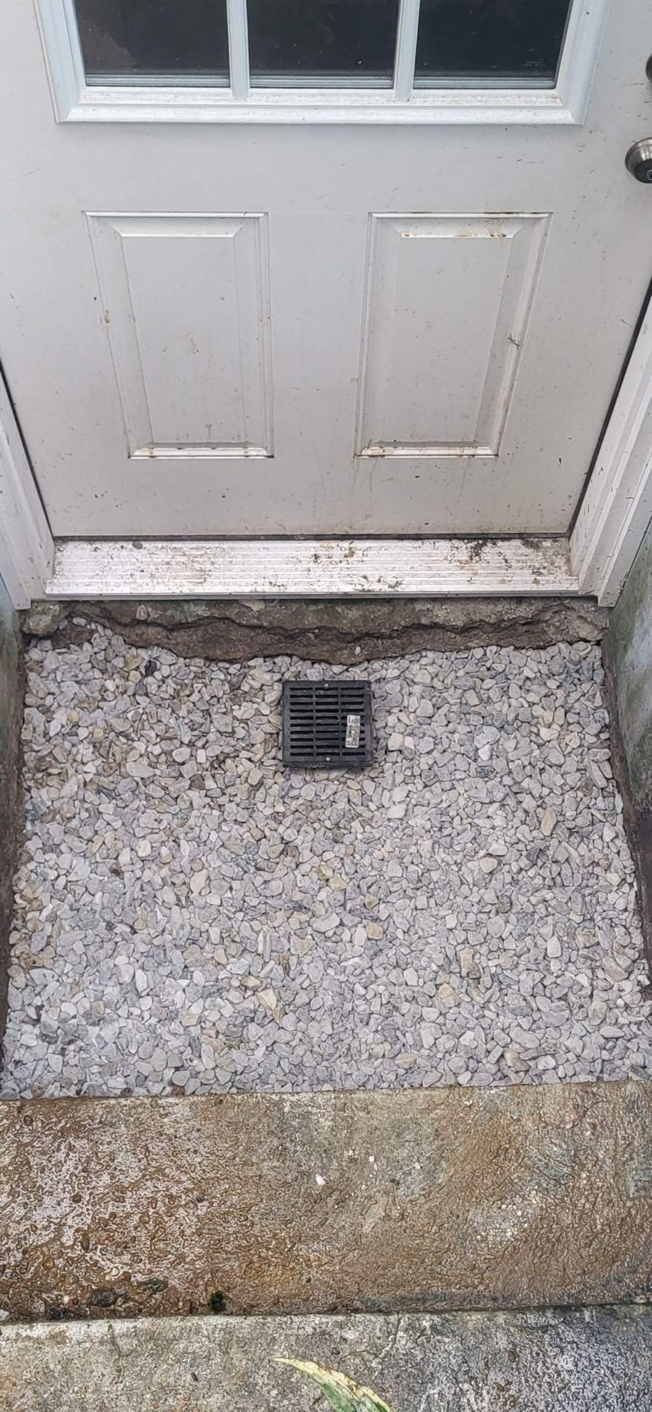 A white door with a drain on the ground next to it
