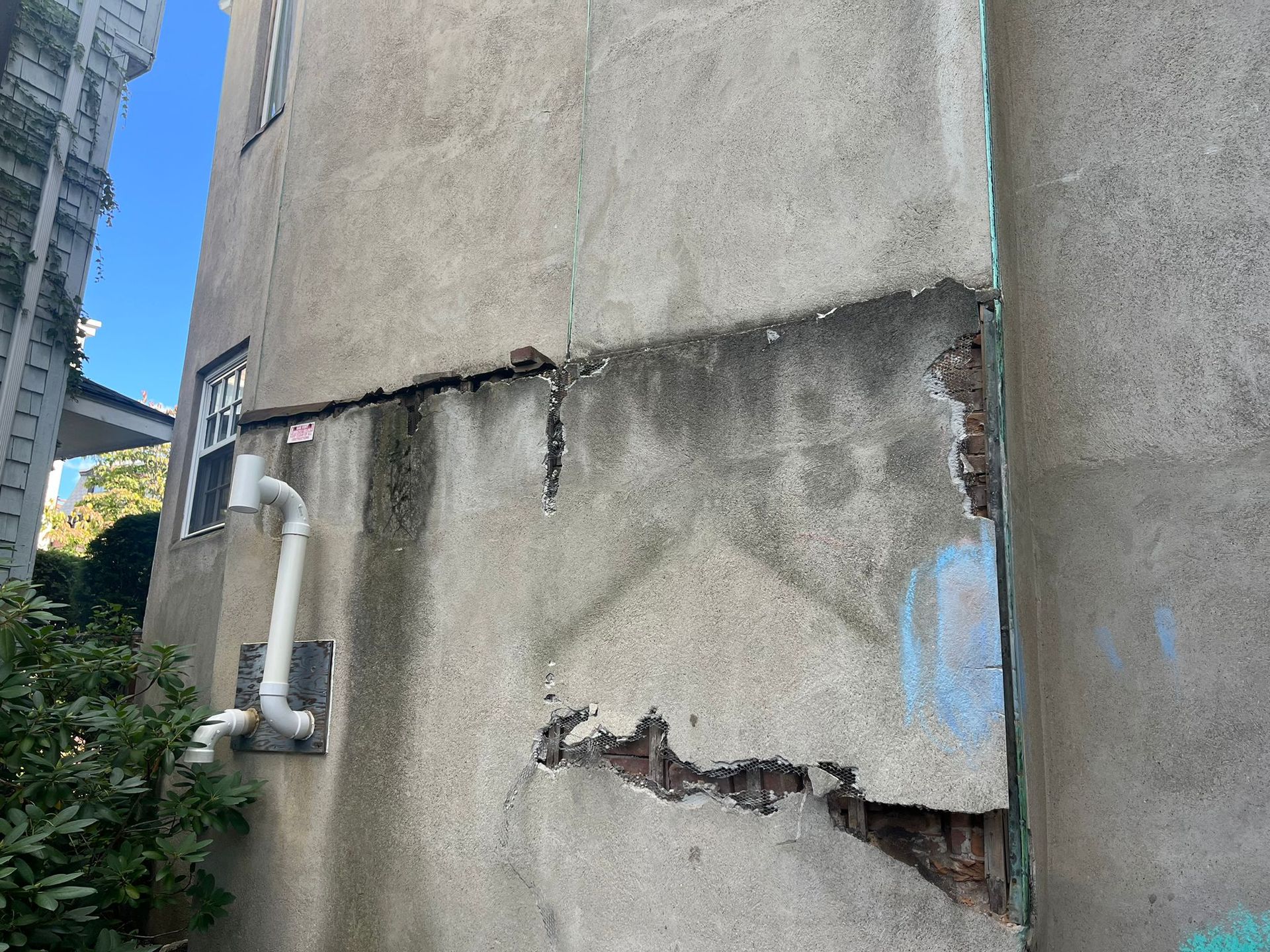 The side of a building with a hole in it and a pipe coming out of it
