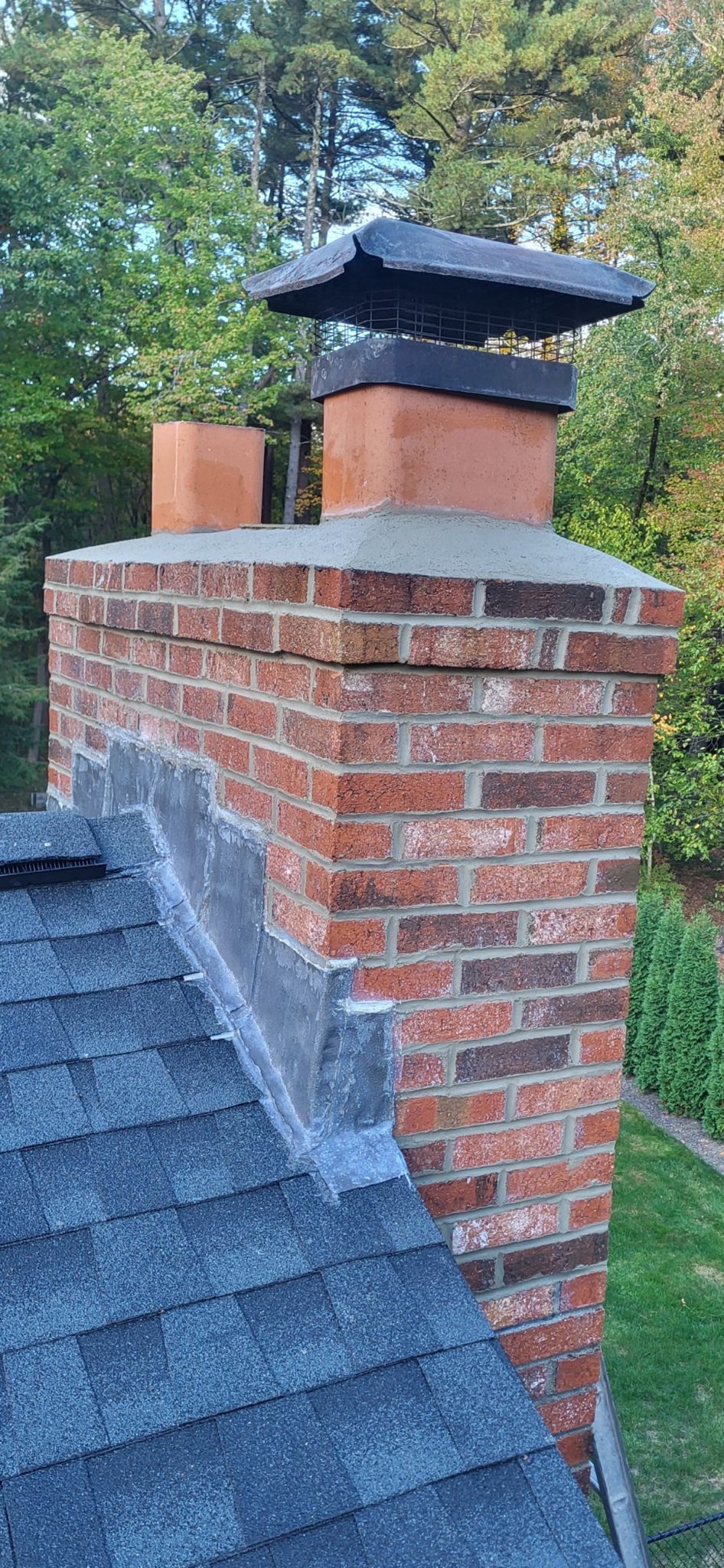A brick chimney on top of a roof with trees in the background