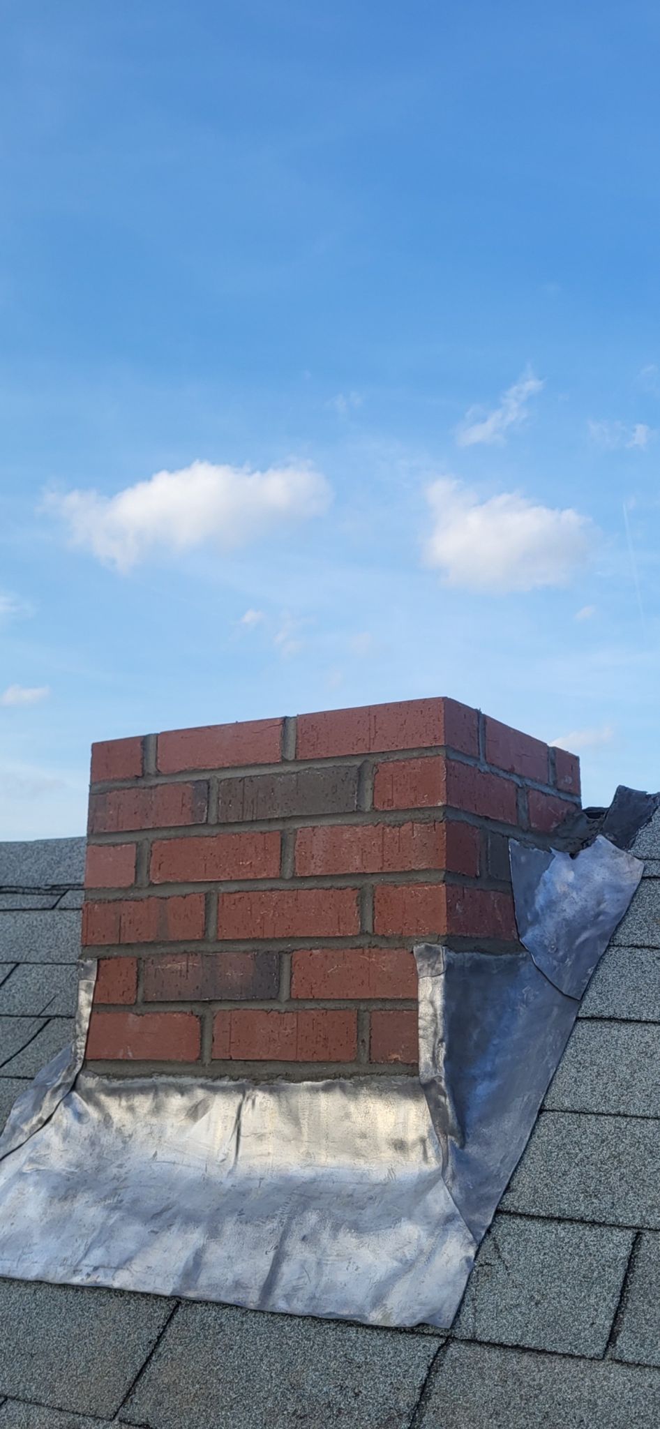 A brick chimney on top of a roof with a blue sky in the background