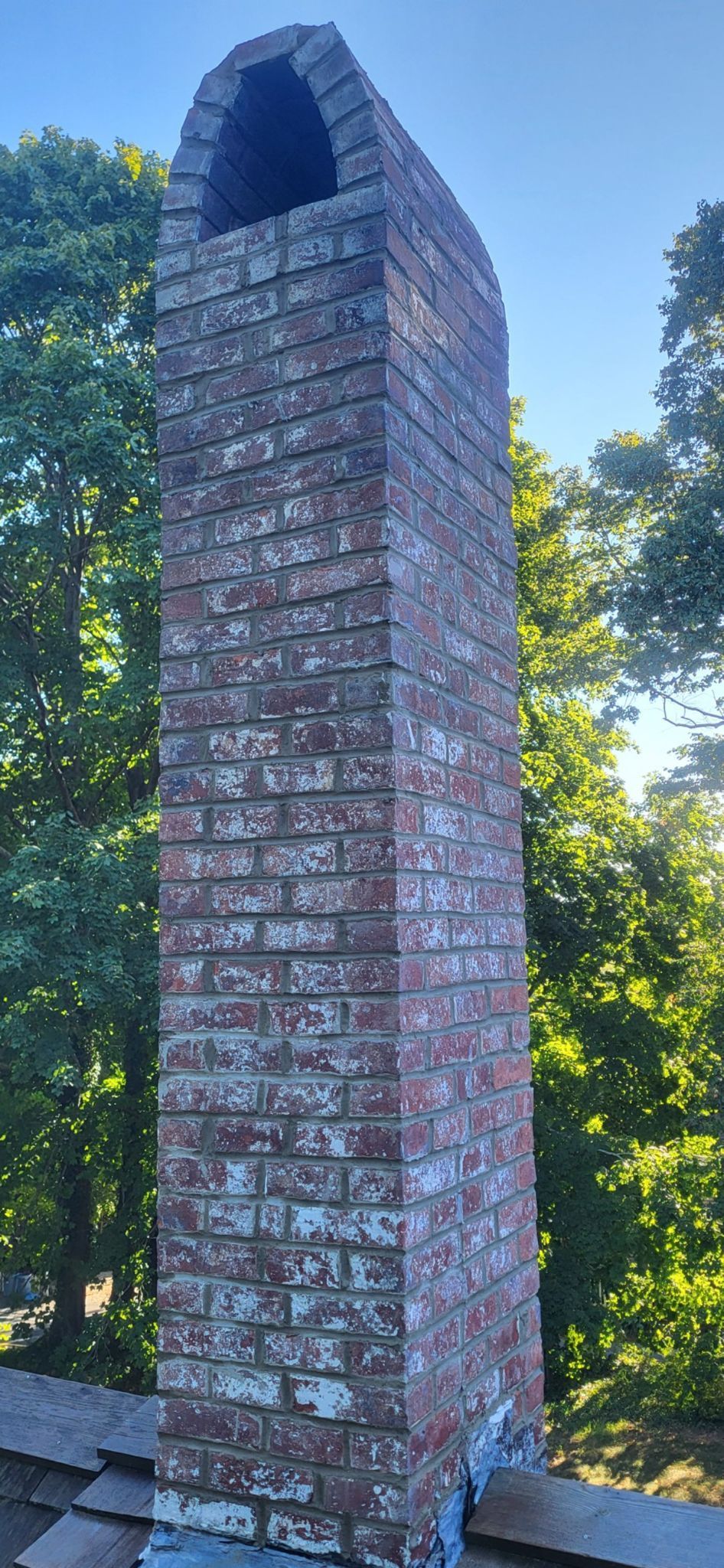 A large brick chimney is sitting on top of a roof surrounded by trees