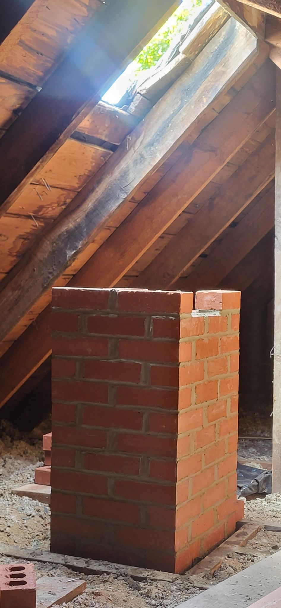 A brick chimney is being built in an attic