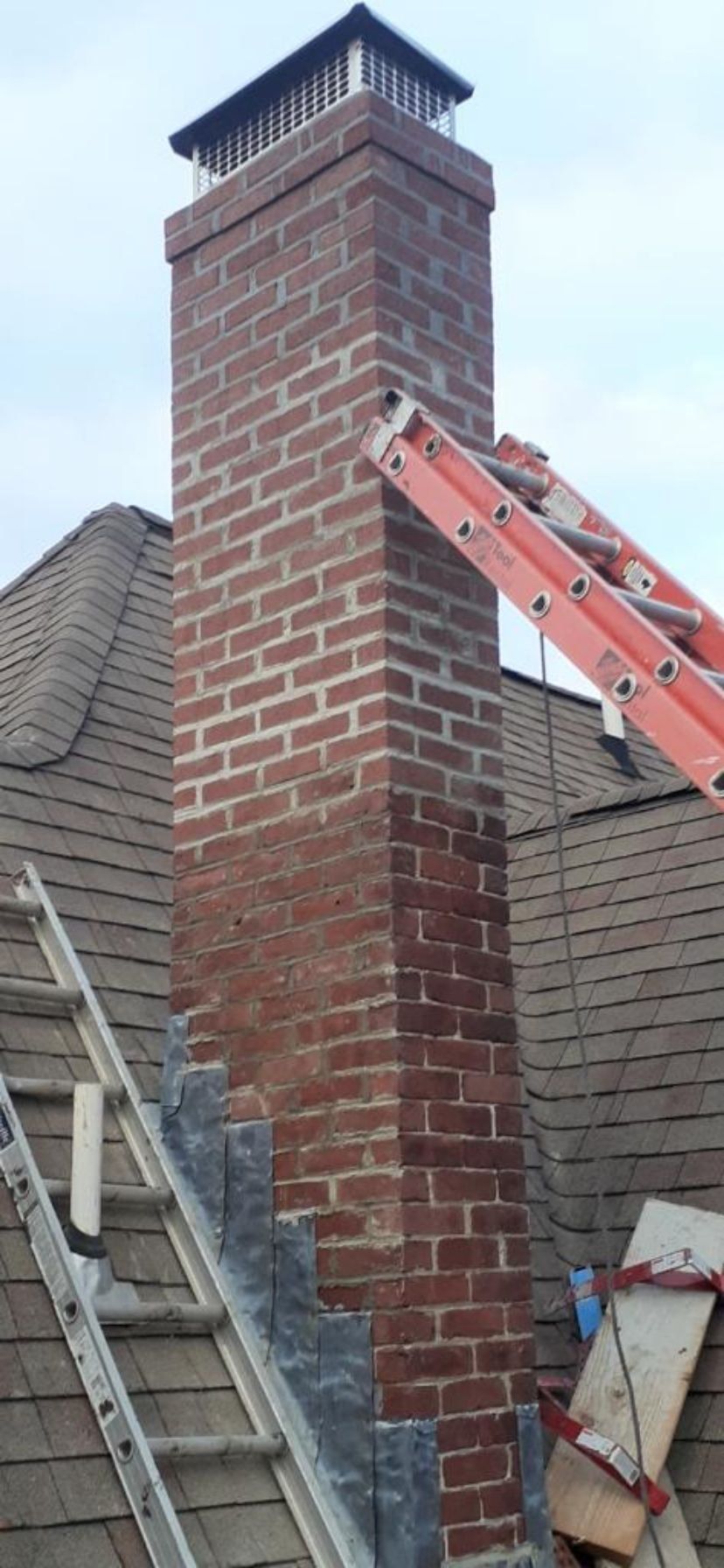 A ladder is leaning against a brick chimney on top of a roof.