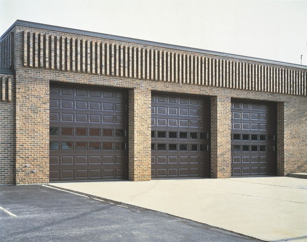 Three garage doors are lined up in front of a brick building