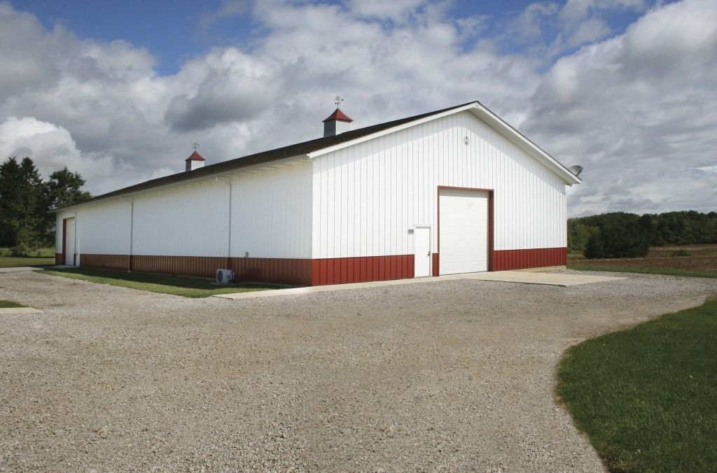 A large white barn with red trim sits on a gravel road