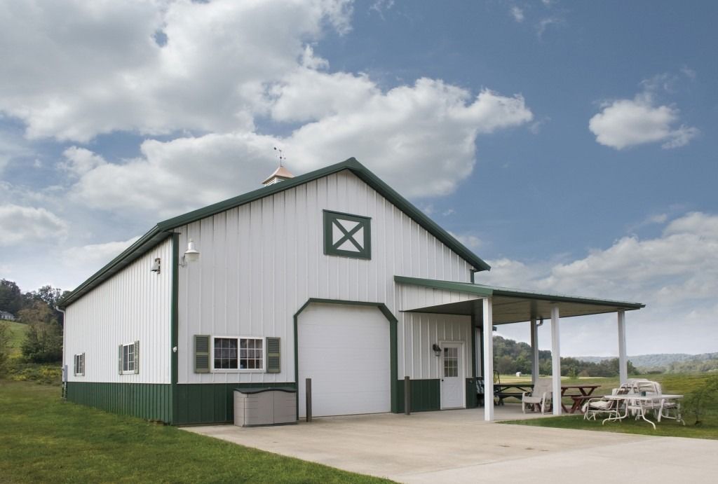 A white and green barn with a picnic table in front of it.