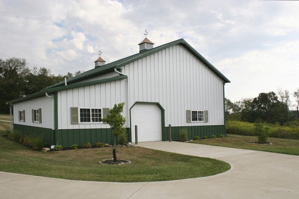 A white and green barn with a concrete driveway in front of it