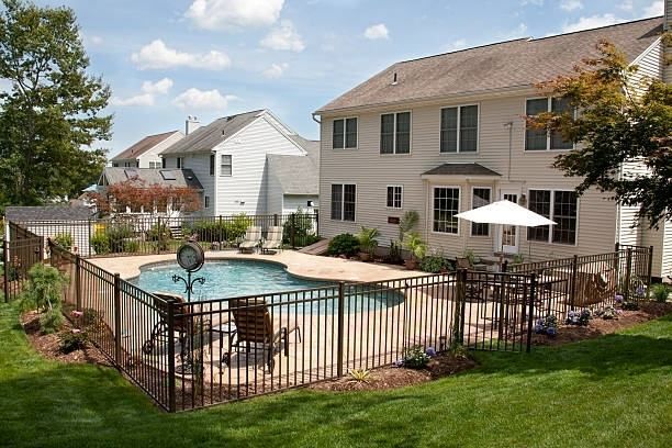 There is a large swimming pool in the backyard of a house with fence