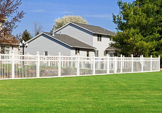 A white fence surrounds a lush green yard in front of a house