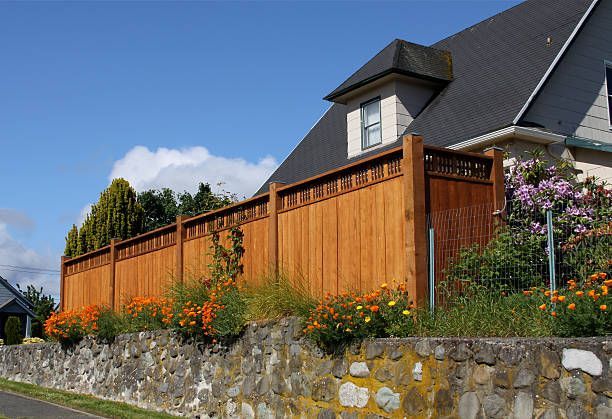 A wooden fence surrounds a stone wall in front of a house