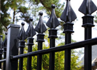 A close up of a black wrought iron fence with trees in the background