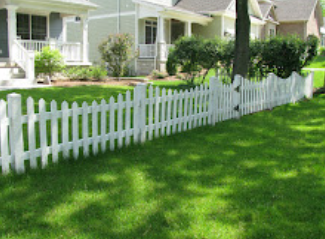 A white picket fence surrounds a lush green lawn in front of a house