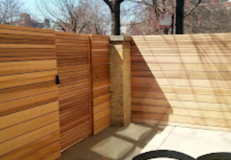 A wooden fence is surrounding a patio with trees in the background