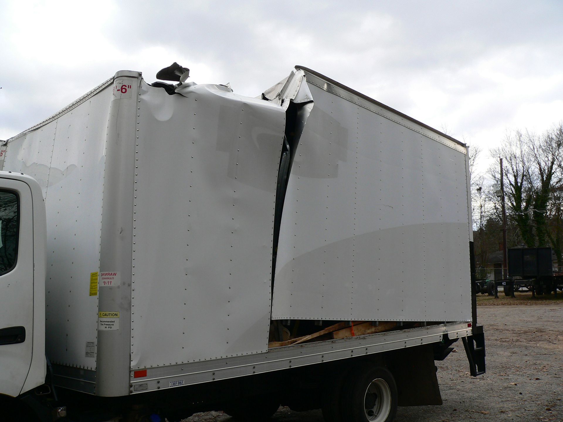 A white truck with a broken side is parked in a gravel lot