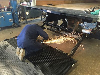 A man is kneeling down and grinding a truck lift gate.