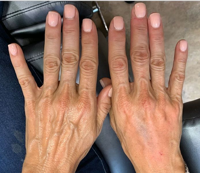 A top-down view of two hands with light pink manicured nails, positioned side-by-side against a dark seat.