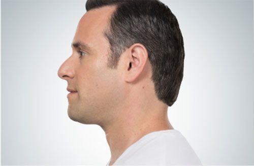 A side profile view of a person with short brown hair against a plain, light gray background.