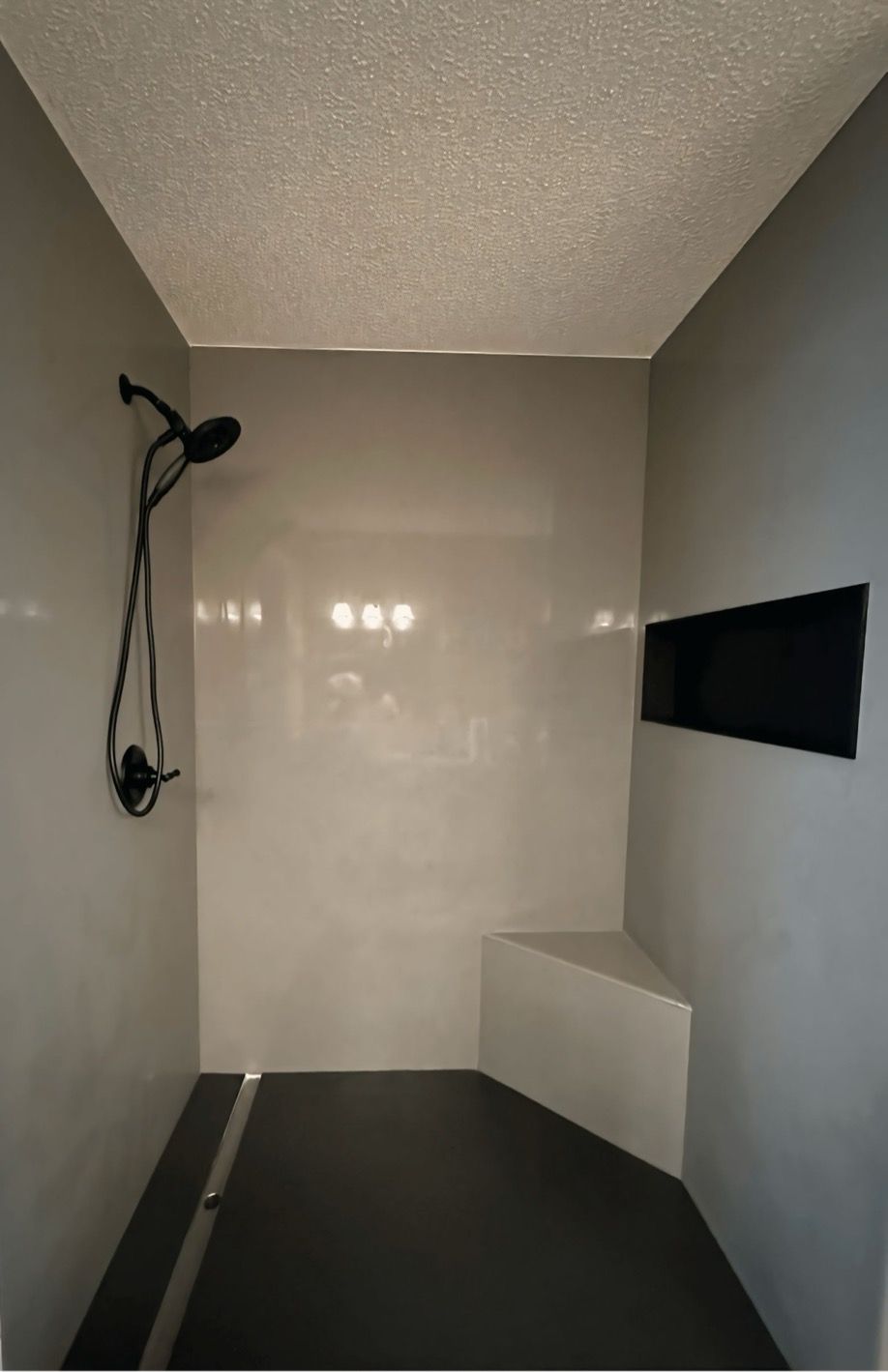 A shower with a black showerhead and a bench