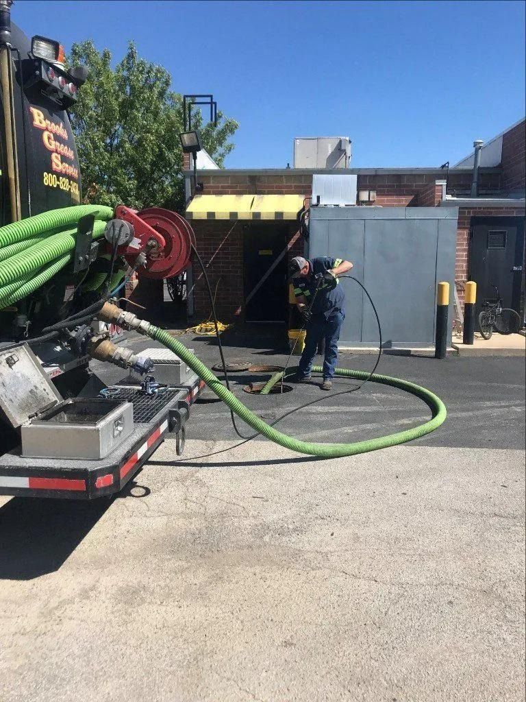 A worker using a vacuum truck to clear a drain pipe on a sunny day.