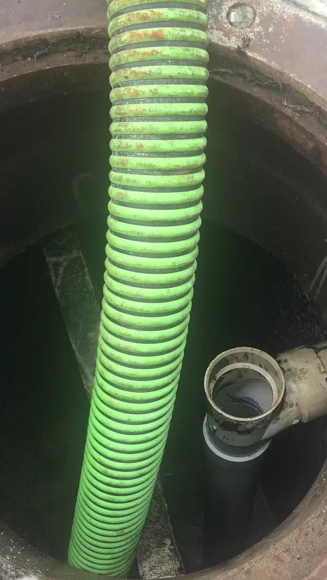 Inside a manhole: green corrugated hose, black pipe, and white pipe fittings.