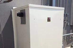 White electrical box mounted on a gray wall with black component and a label.