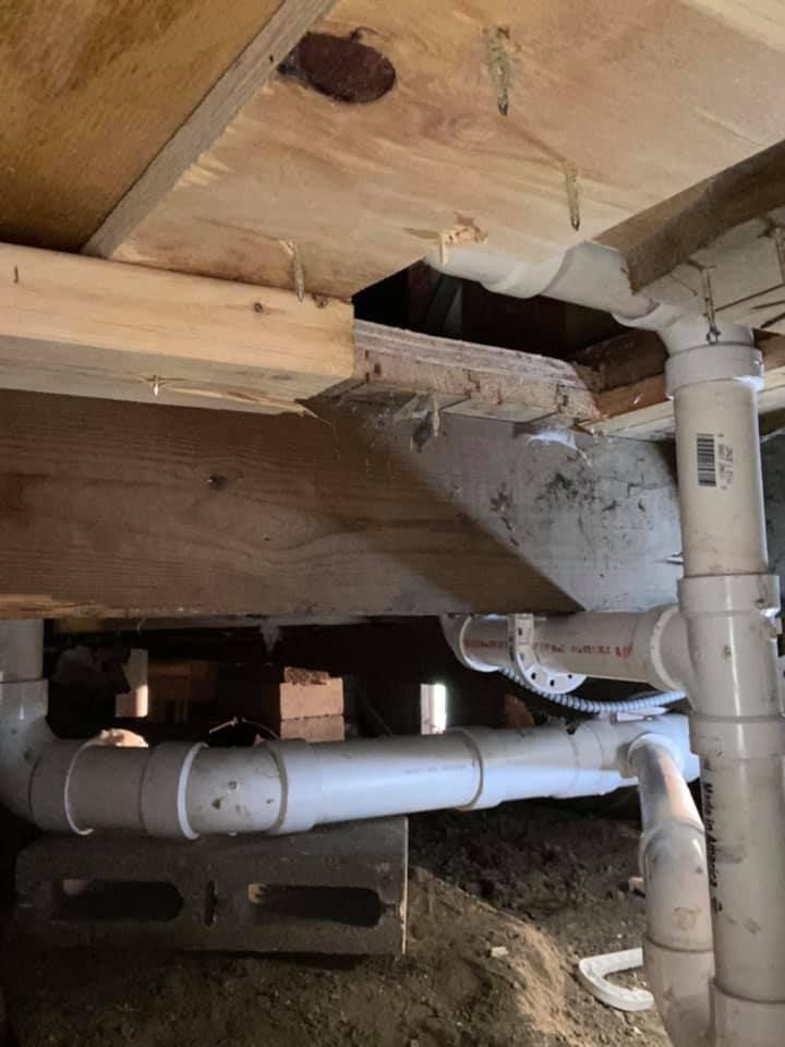 A bathroom sink is under a wooden floor with pipes coming out of it.