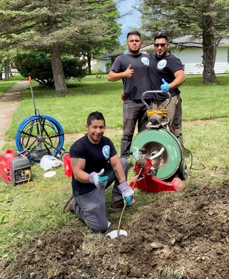 Three men are kneeling in the dirt next to a machine.