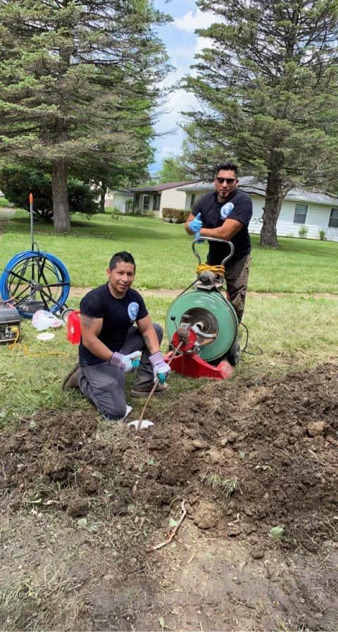Two men are kneeling in the dirt with a machine in a field.