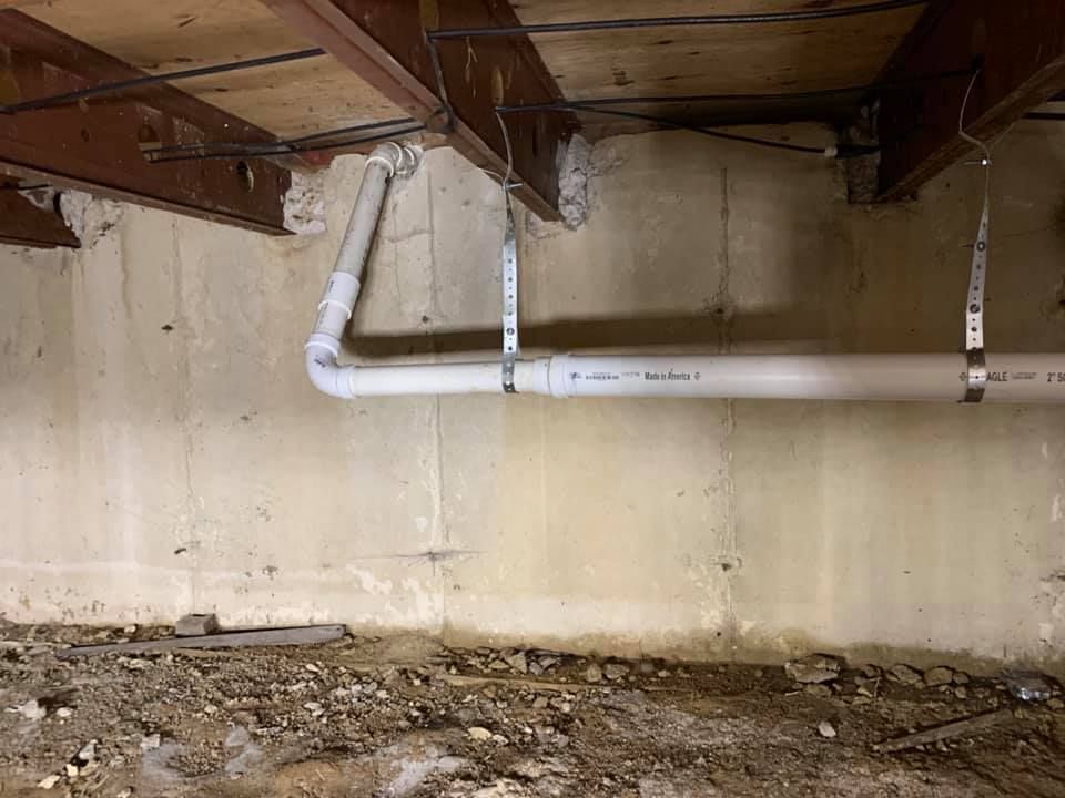 A white pipe is hanging from the ceiling of a basement.