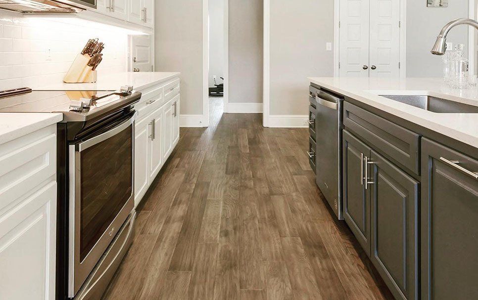 A kitchen with hardwood floors , stainless steel appliances , and white cabinets.