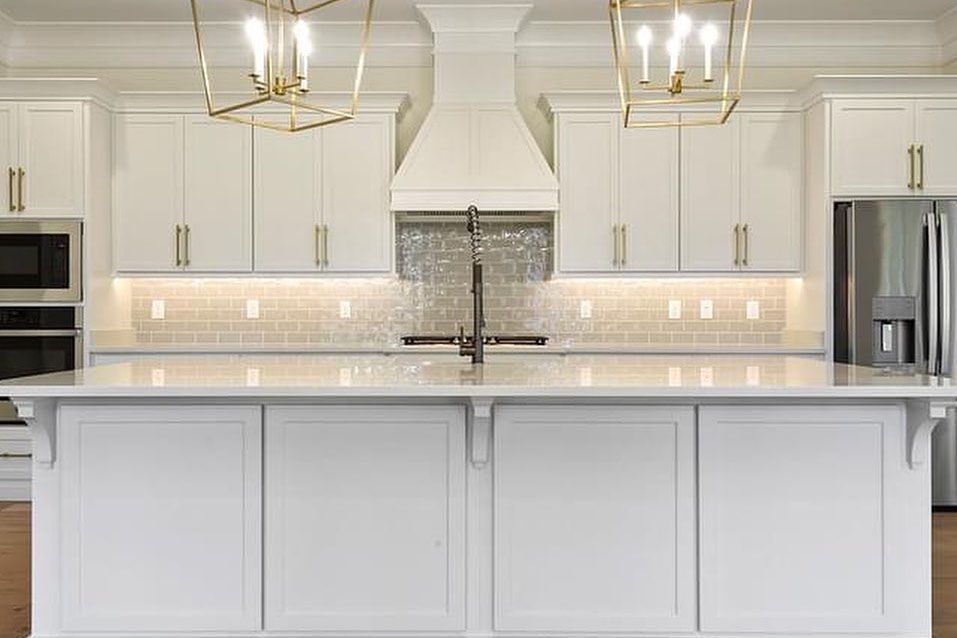 A kitchen with white cabinets , a large island , a sink , and a refrigerator.