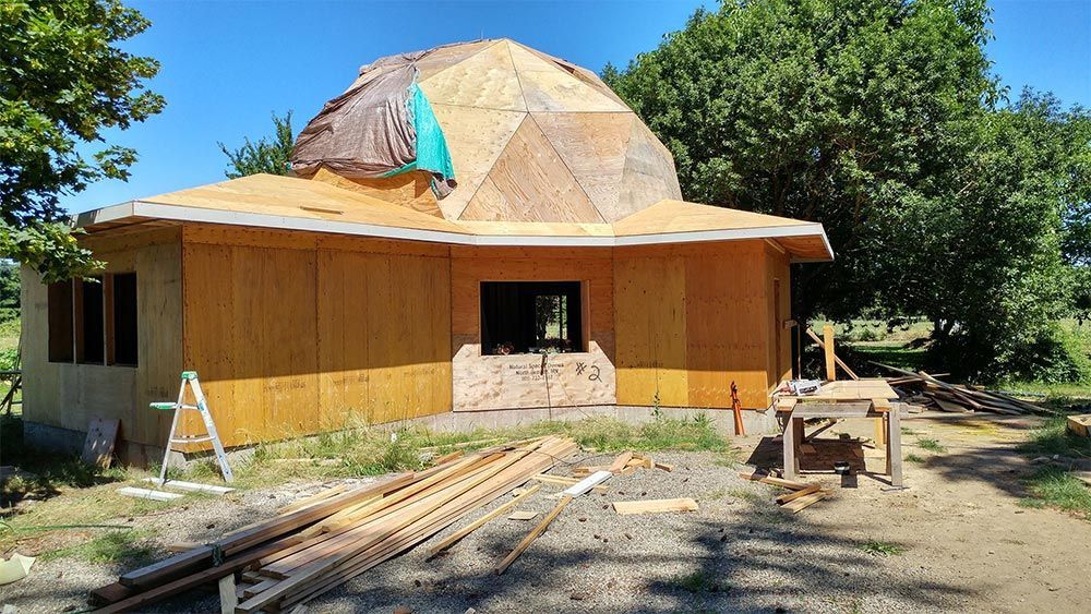 A dome shaped house is being built in the middle of a field.