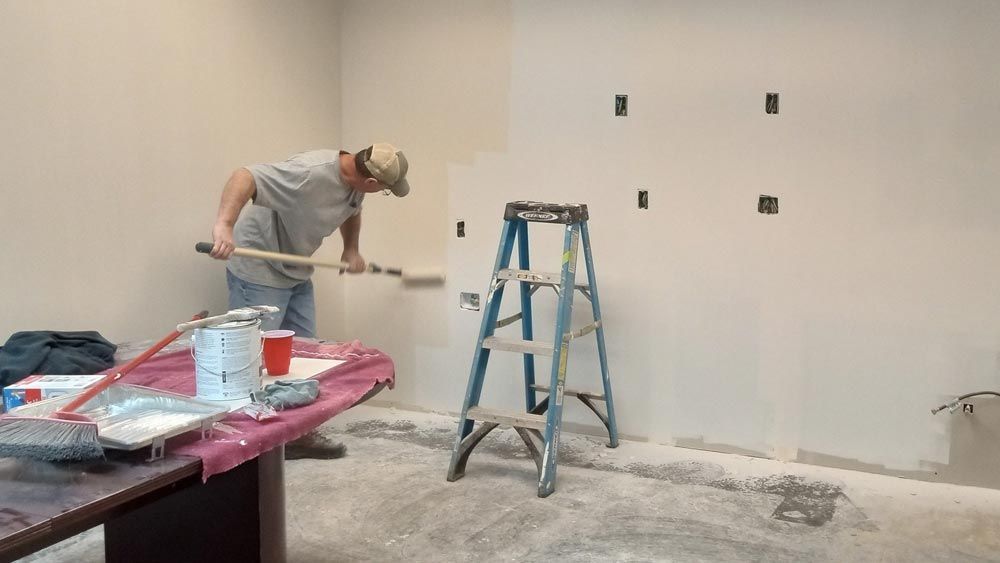 A man is painting a wall in a room with a ladder in the background.