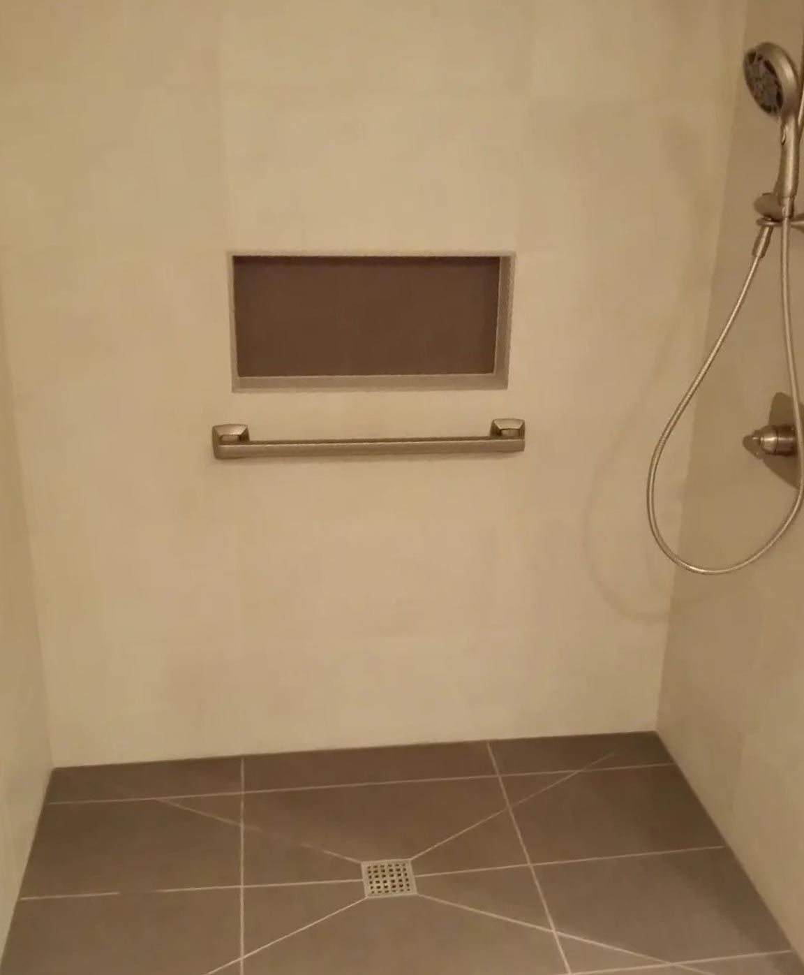 A walk in shower with a hand rail and a shower head.