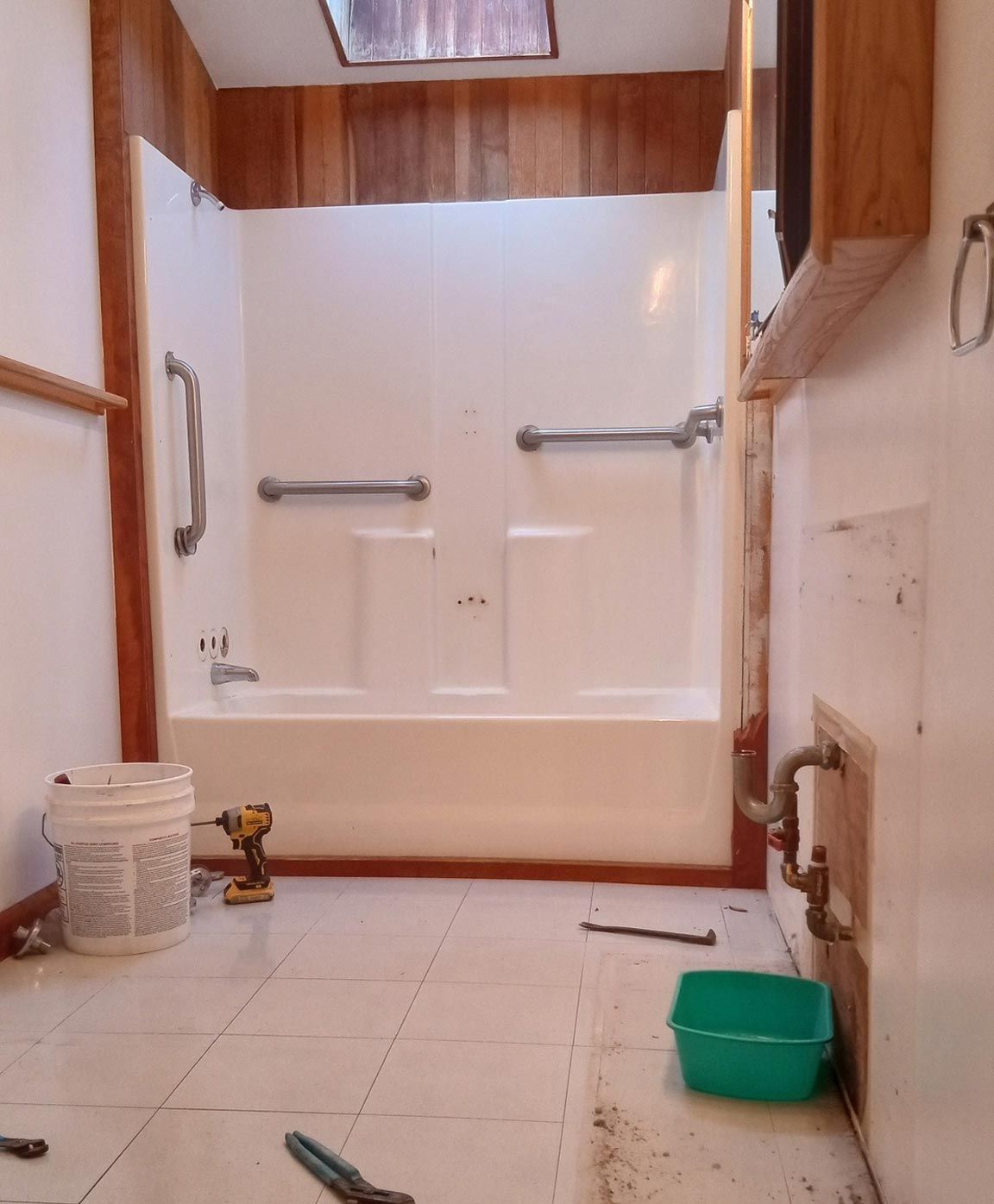 A bathroom with a bathtub and a green bucket on the floor