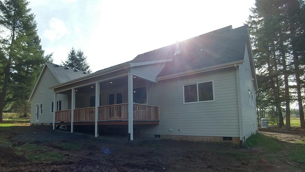 The back of a house with a porch and trees in the background