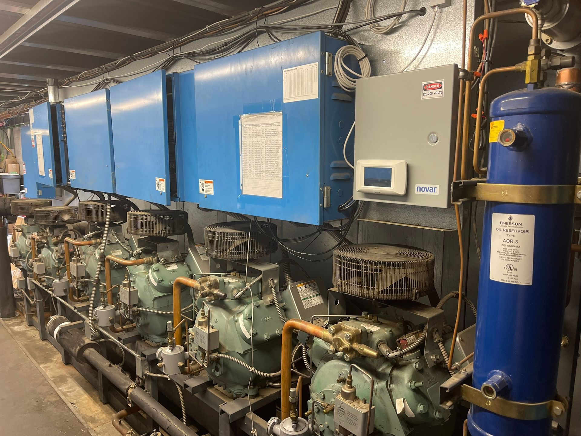 Industrial machinery room with blue compressors, pipes, and tanks along a wall